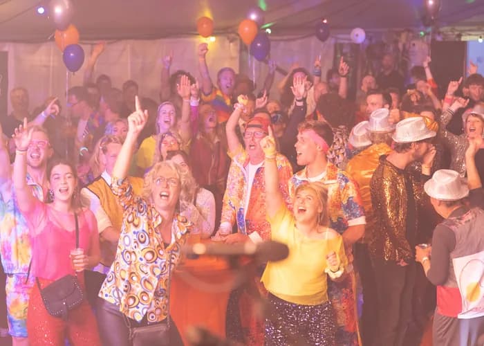 Feesttent vol publiek met een podium vol ballonnen en een kleurrijke lichtshow van QuizX.