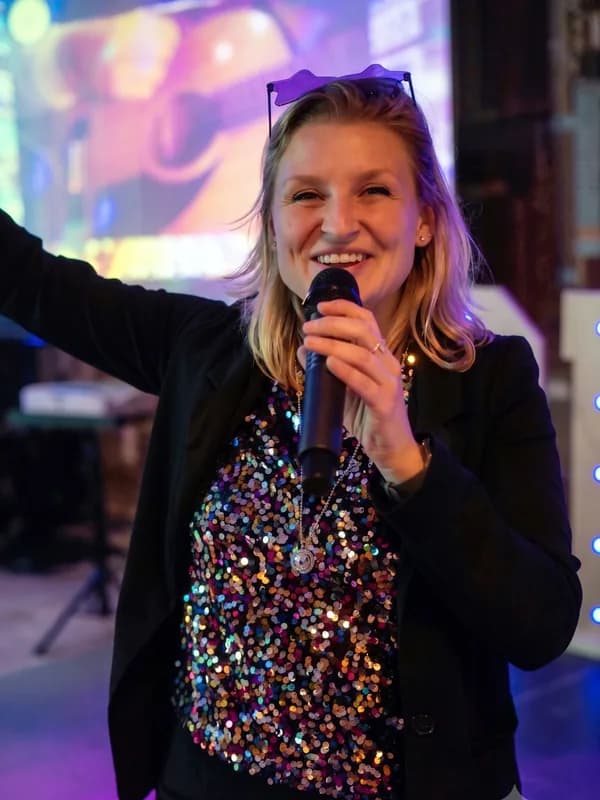 Presentatrice Linda met glittertop Enthousiaste presentatrice Linda met zonnebril en kleurrijke pailletten top jubelt met een microfoon in de hand.