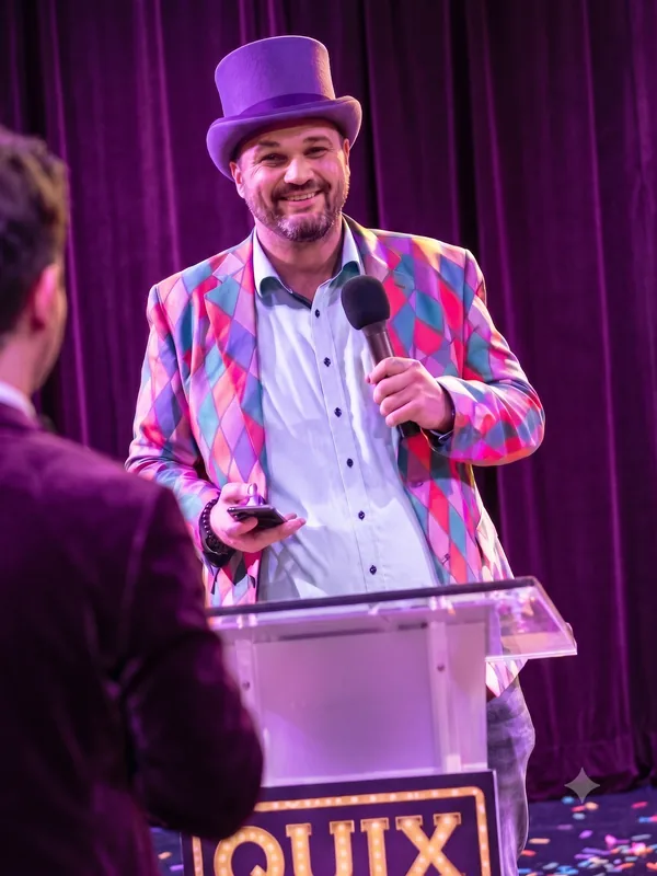 Quizmaster met paarse hoge hoed Quizmaster met een paarse hoge hoed en kleurrijk ruit-colbert achter de QuizX-lessenaar tijdens een quizshow.
