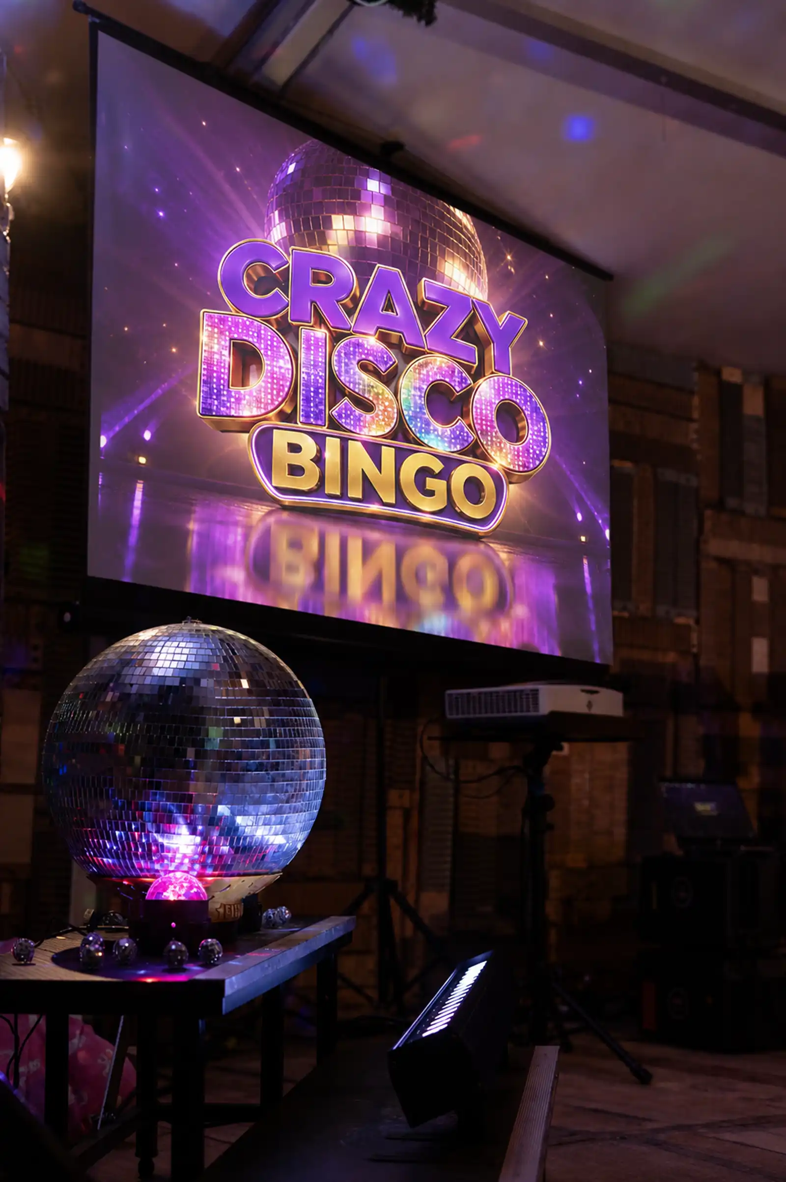 Sfeervolle opstelling met discobal en verlichting voor aanvang van de show. Discobal reflecteert sfeervol licht op een houten tafel voor een presentatiescherm tijdens een feestavond.