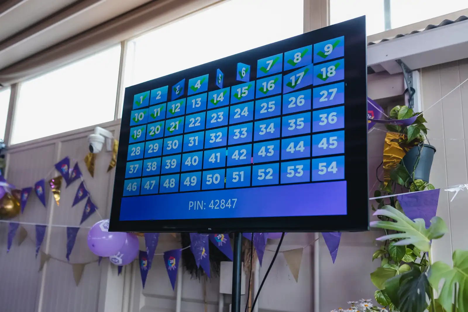 Centraal scherm met de spel-PIN waarmee teams eenvoudig kunnen inloggen op de quiz. Groot digitaal scherm met nummers en een PIN-code tijdens een interactief evenement in een versierde zaal.