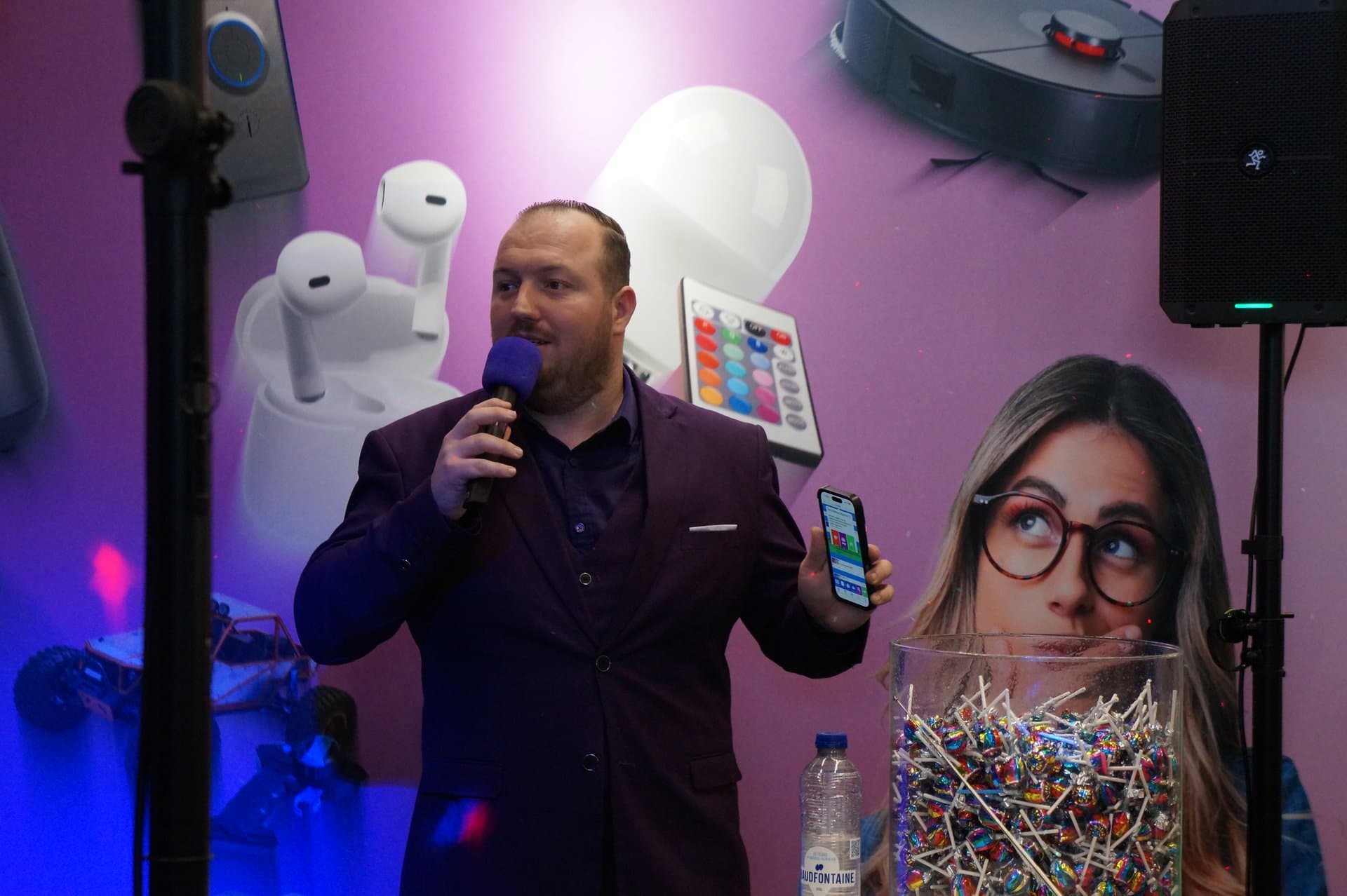 Muziekbingo presentator paars pak Quizmaster in paars pak presenteert een vraag via zijn smartphone tijdens een muziekbingo, voor een paars decor met elektronica.