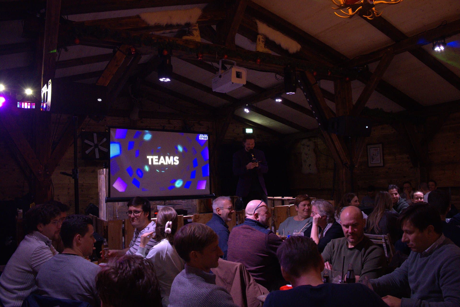 Pubquiz voor bedrijven teams in de startblokken Teams bereiden zich voor op de eerste ronde van een pubquiz voor bedrijven, onder leiding van de quizmaster in een gezellig volle zaal.