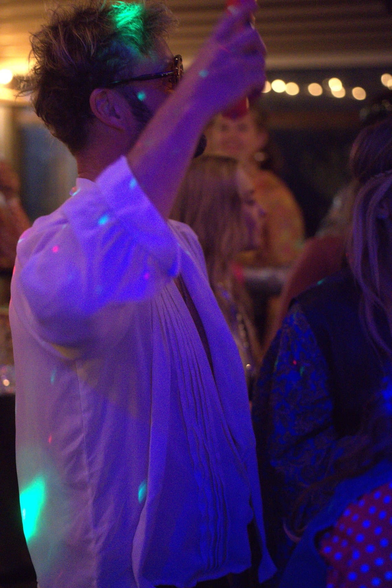 Pubquiz voor bedrijven dansje met discolicht Dansende deelnemer heft het glas tijdens een pubquiz voor bedrijven, met discolichten die kleurrijk reflecteren op de feestelijke kleding.