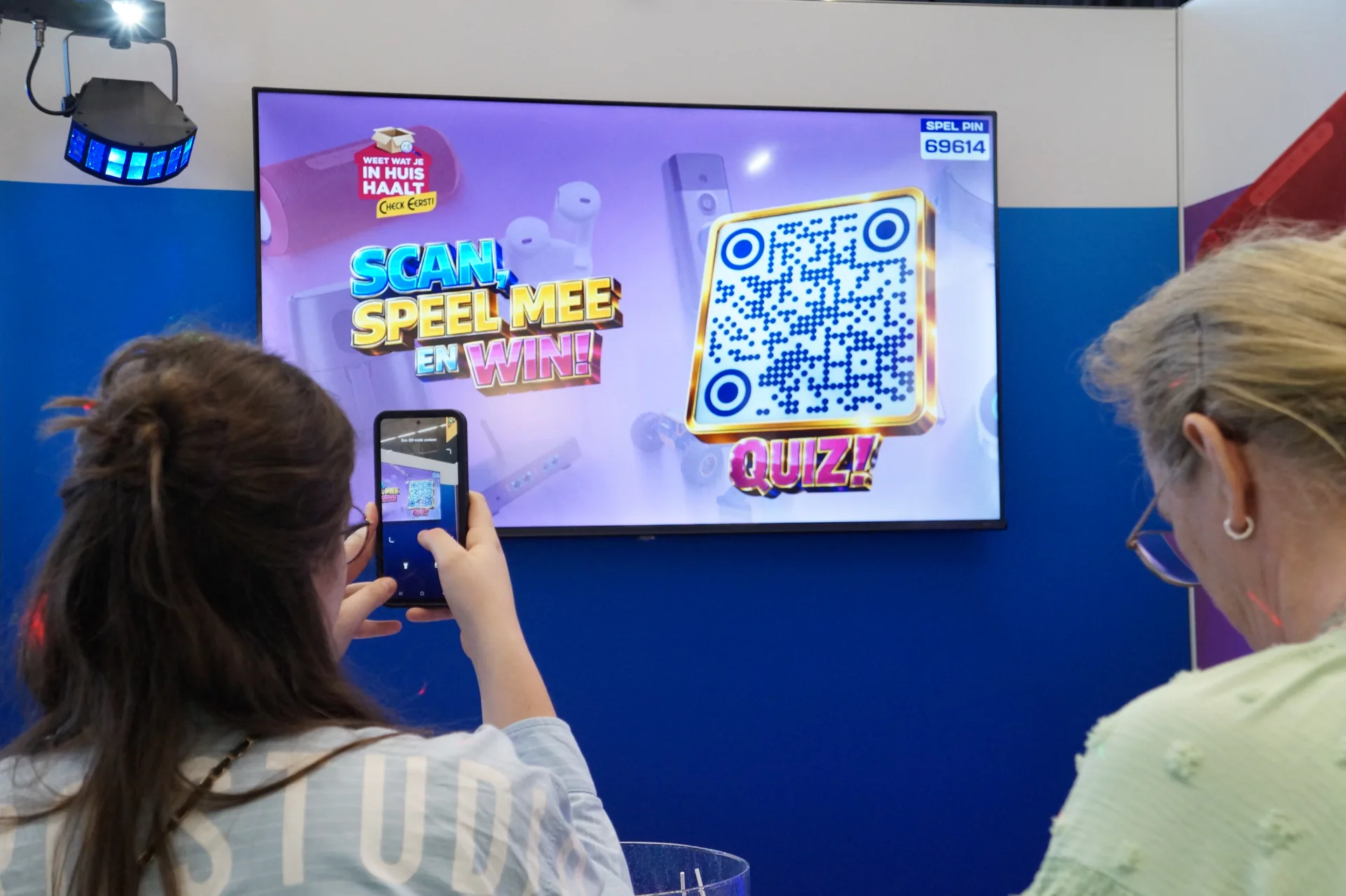 Bezoeker scant met haar telefoon de QR-code op het quizscherm: scan, speel mee en win