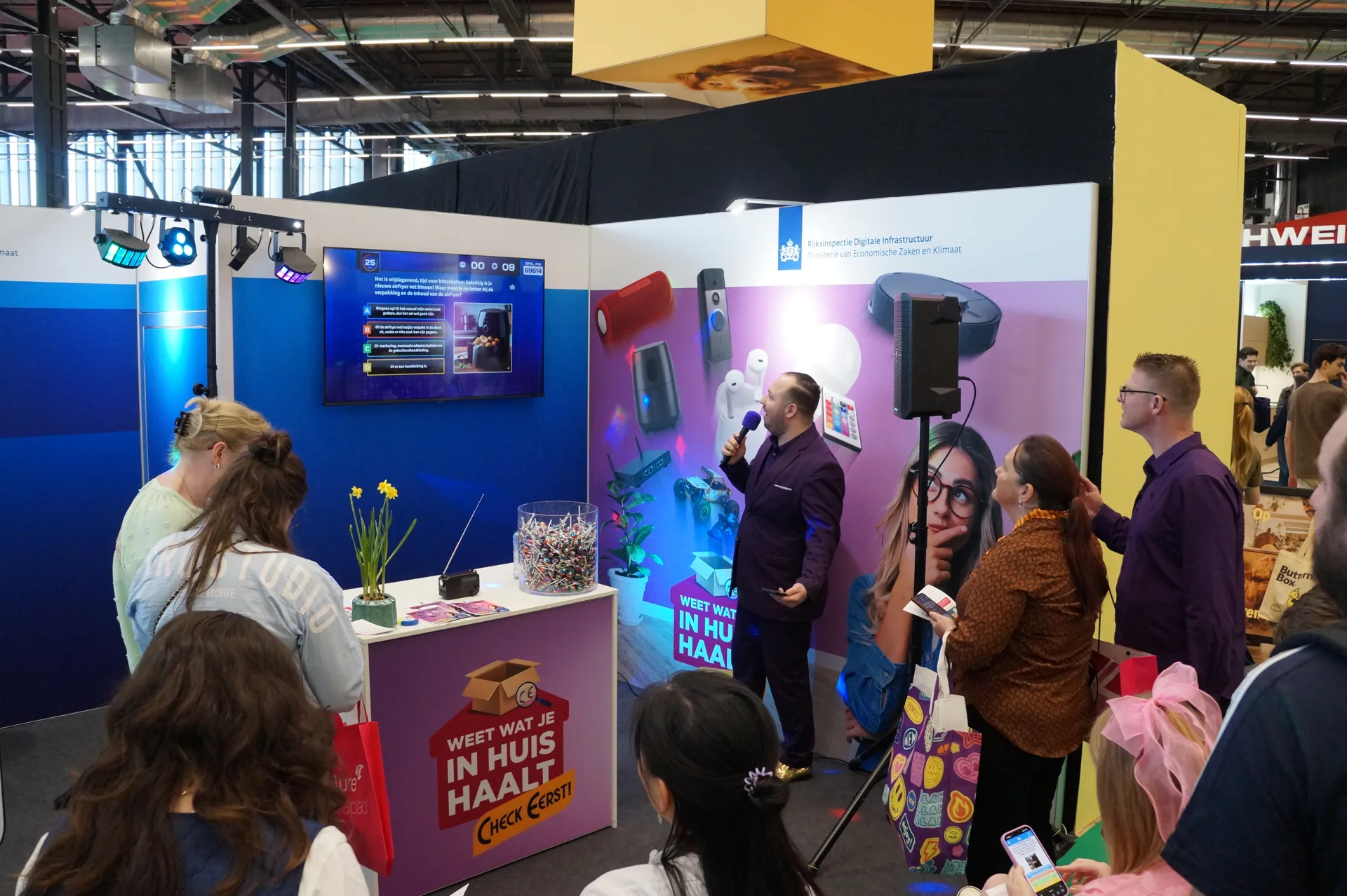 Quizmaster met microfoon op de RDI-stand terwijl bezoekers meespelen op hun telefoon, Huishoudbeurs 2026