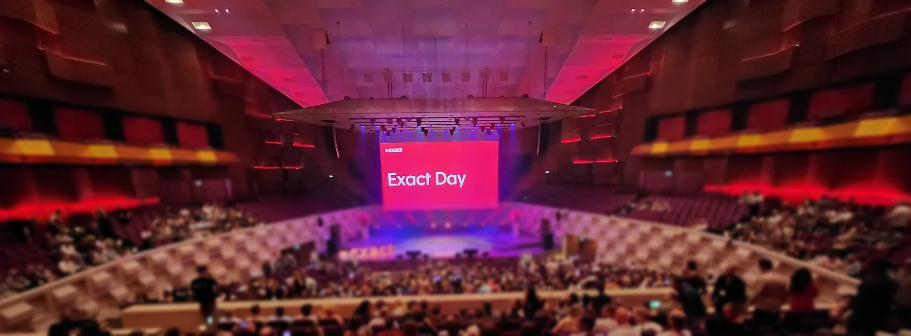 De Grote Zaal van De Doelen in Rotterdam vol collega's van Exact tijdens Exact Day, met Exact Day op het grote scherm boven het podium