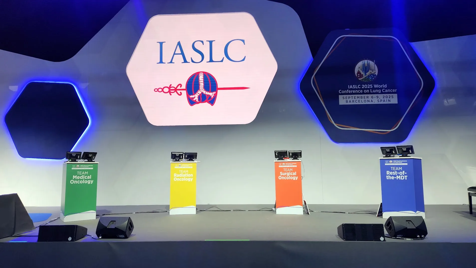 Vier kleurgecodeerde teamdesks in WCLC-huisstijl op het podium van Fira Barcelona, 2025