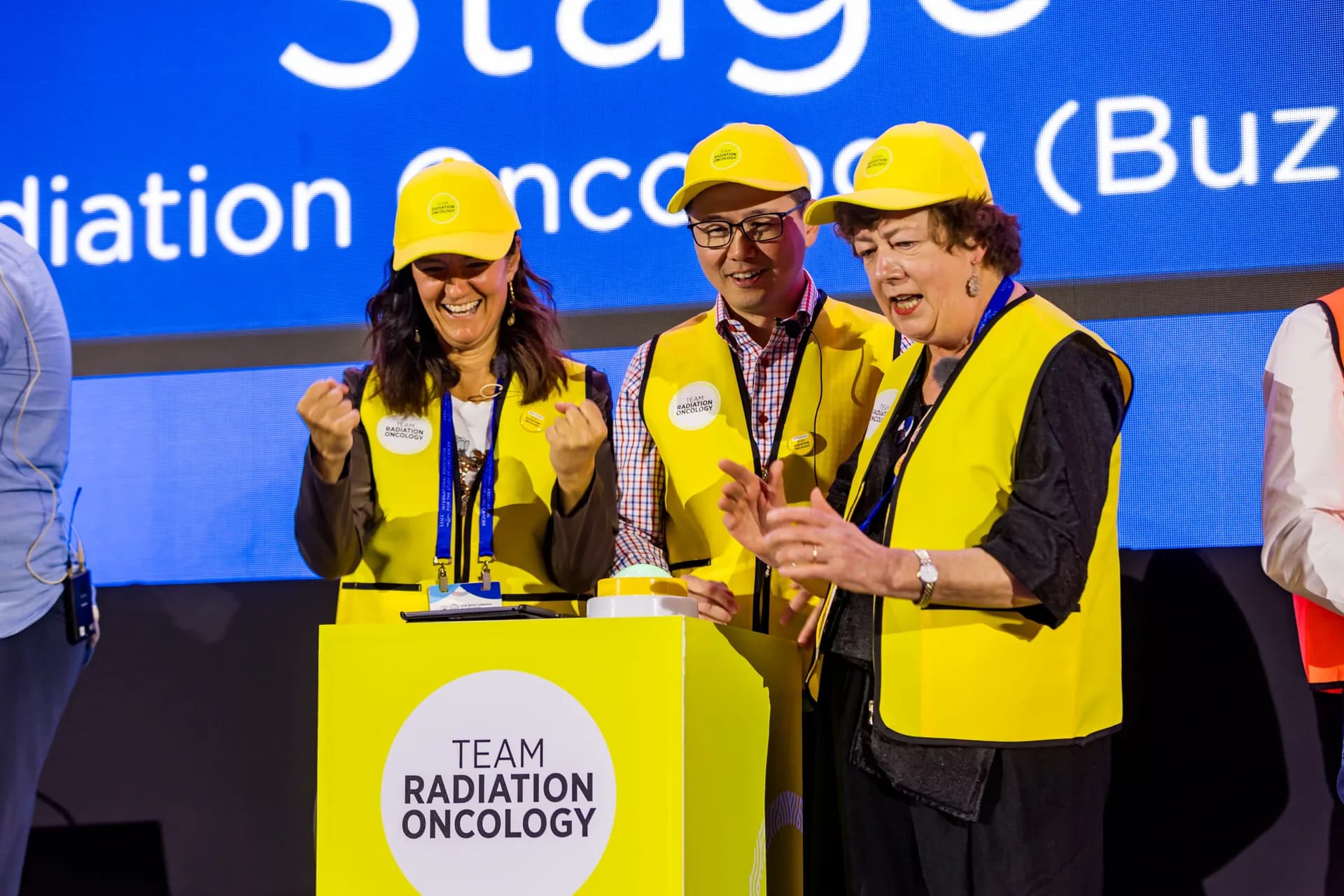 Team Radiation Oncology in gele hesjes juicht achter de buzzer op het podium in Seoul