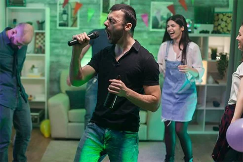 Groep vrienden geniet van een karaoke feestje in een woonkamer, met een man die enthousiast in een microfoon zingt.