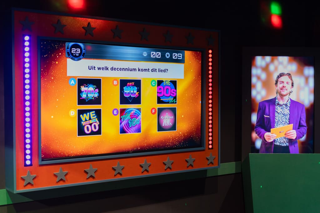 Quizscherm met vraag over muziekdecennia in de QuizXarena quizroom, vergezeld door een afbeelding van de quizmaster in paarse jas.