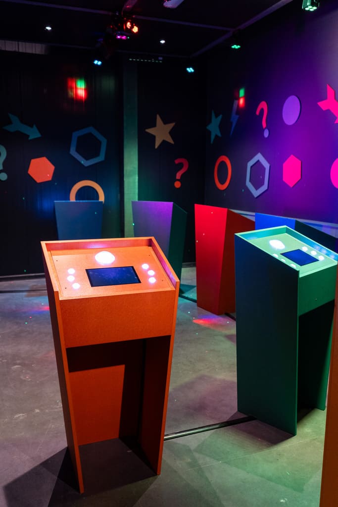 Interactieve kleurrijke quizruimte in QuizXarena met meerdere spelterminals en levendige geometrische decoraties.