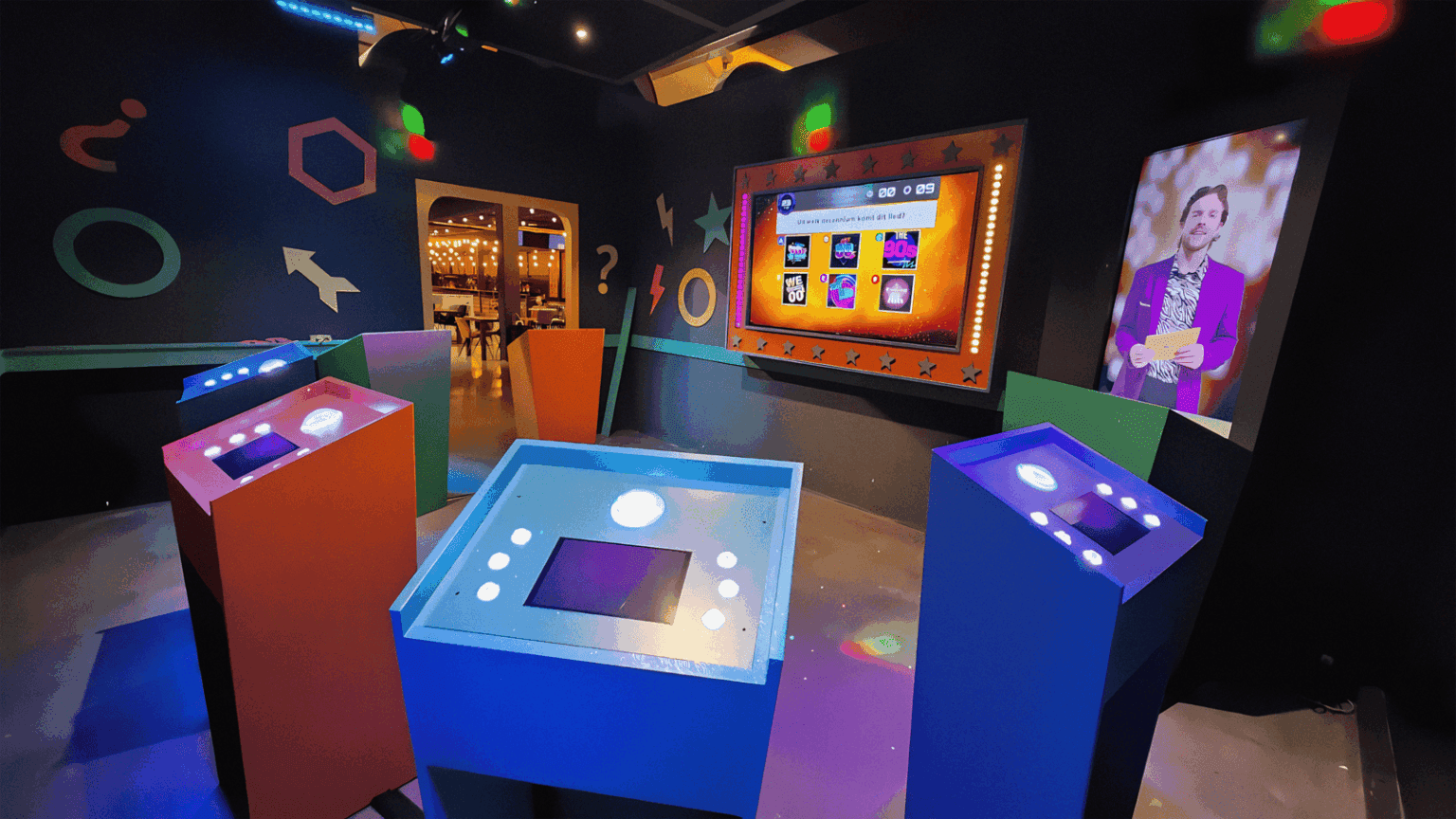 Interactieve spelopstelling met kleurrijke consoles en groot quizscherm in QuizXarena quizroom, met energieke verlichting en geometrische decoraties.