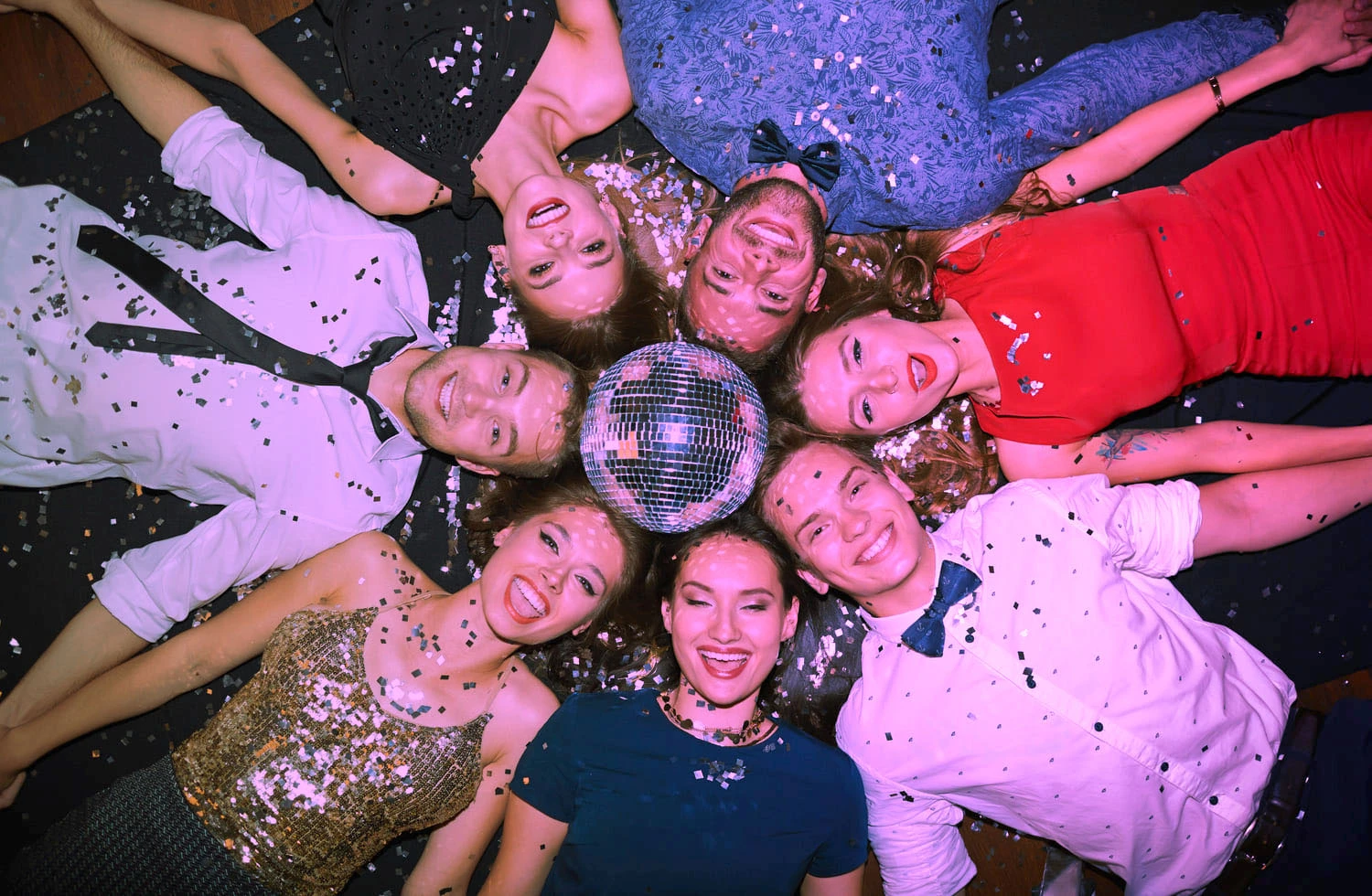 Vrolijke groep mensen liggend in een cirkel met een disco-bal en confetti, genietend van een Crazy Disco Bingo.