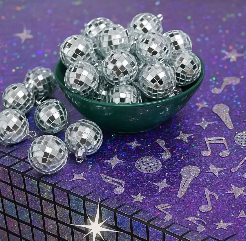 Feestelijke tafeldecoratie met zilveren discobal ornamenten in een groene schaal op een paarse ondergrond met muzikale symbolen en glitters, ideaal voor een tafeldecoratie pakket quizx.