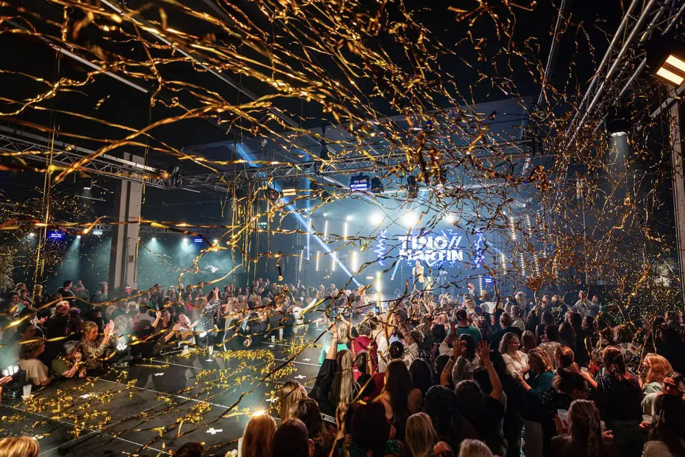 Feestelijke sfeer met gouden confetti en enthousiaste menigte op het Trio Latino evenement, in de context van een gepersonaliseerde pubquiz ervaring