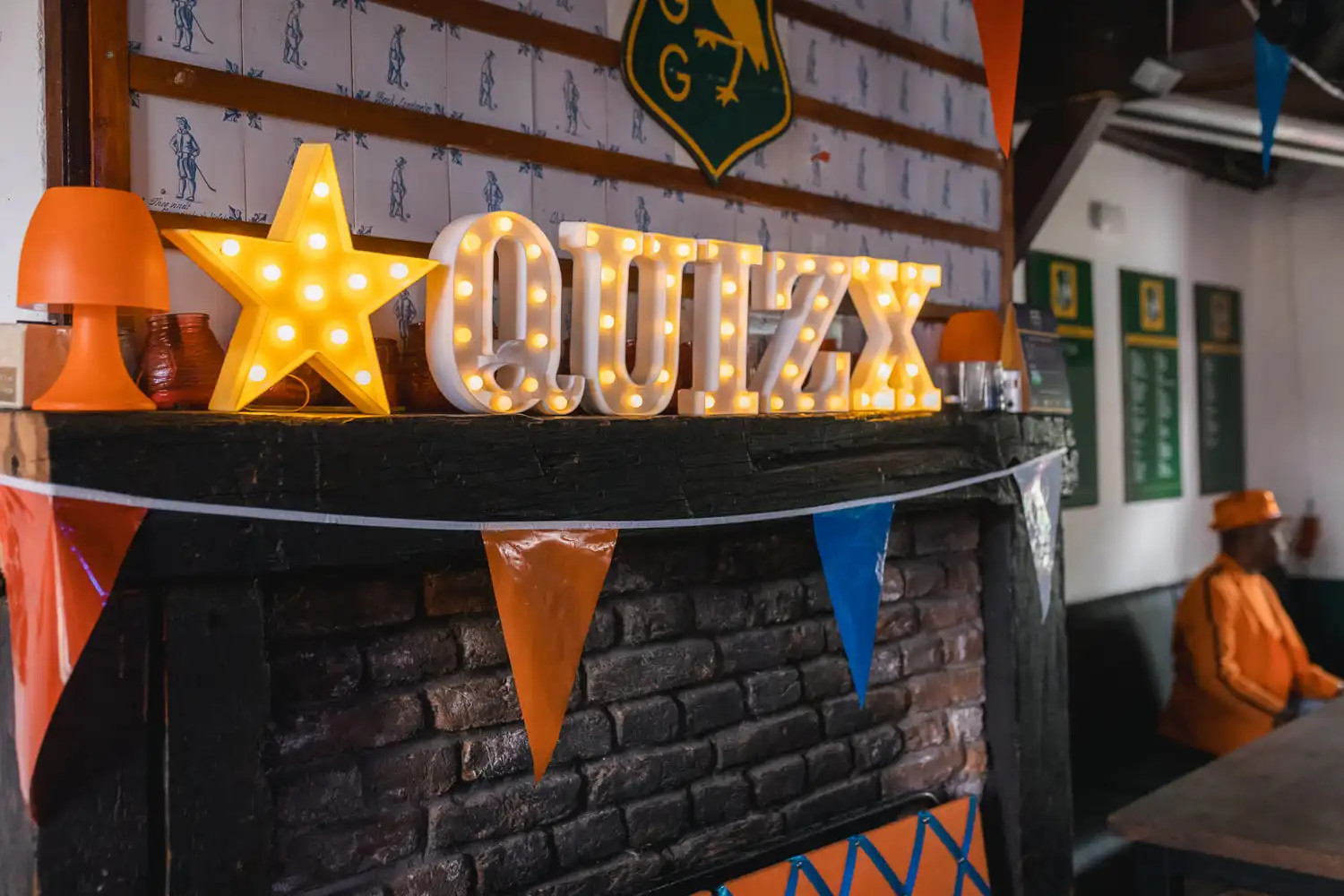 Feestelijke versiering met verlichte 'QUIZ' letters en oranje vlaggetjes, typerend voor een 'Ik hou van Holland' quizavond.
