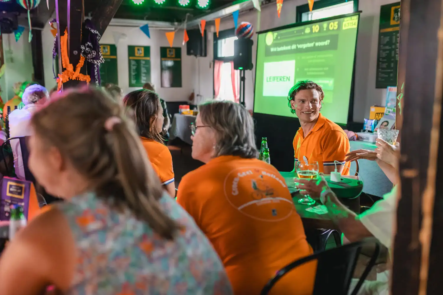 Groep mensen in oranje shirts genietend van een Ik hou van Holland quiz avond in een feestelijk versierde ruimte.