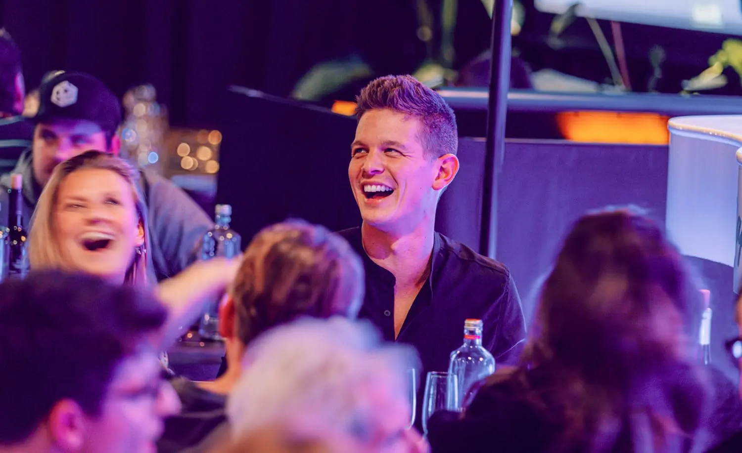 Lachende mensen tijdens een pubquiz evenement in een gezellige binnenomgeving met flessen op tafel, ideaal voor een pubquiz inhuren.