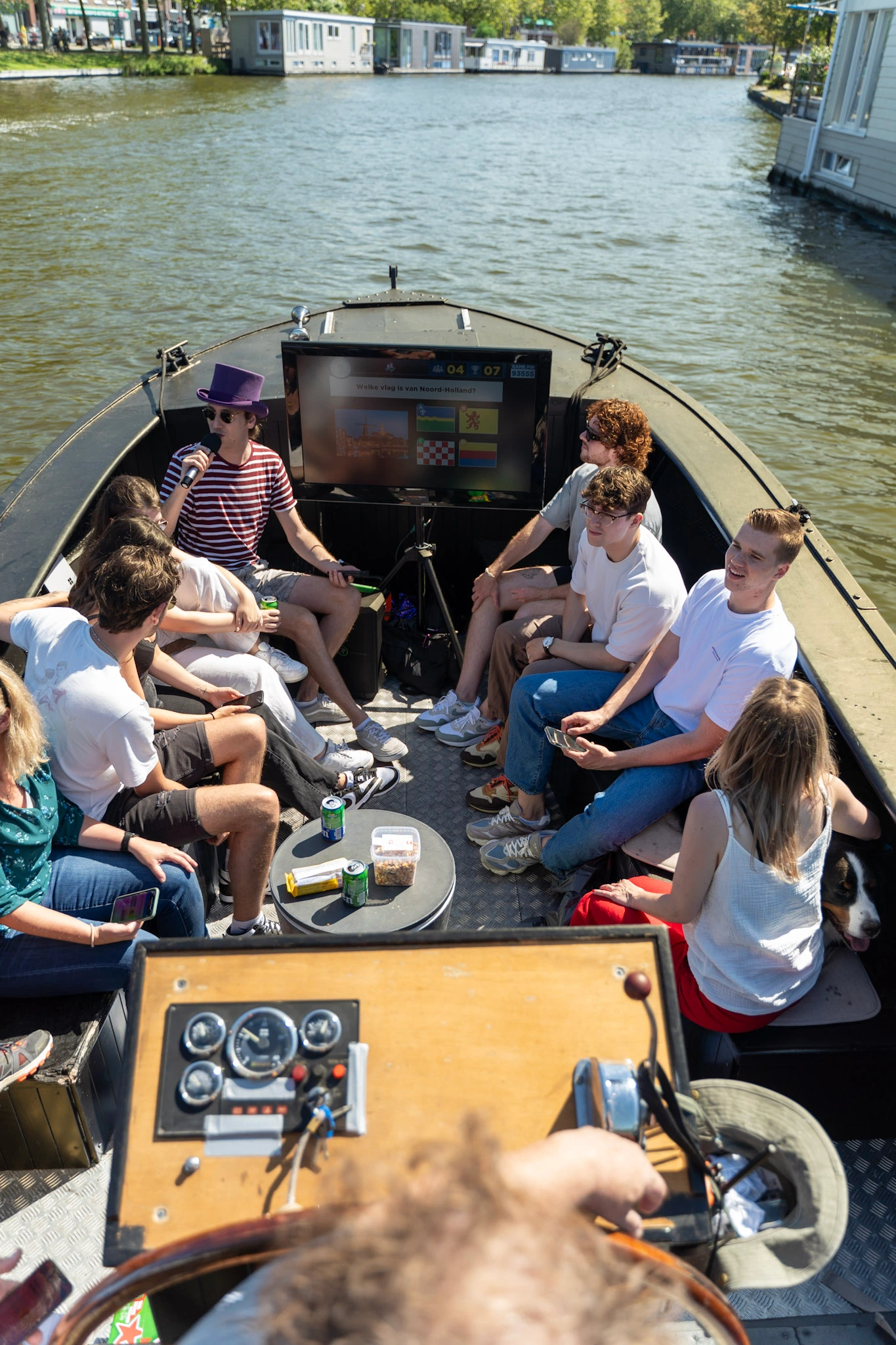 Groep mensen speelt een pubquiz op een boot in Den Haag, met een quizvraag op een scherm en een ontspannen sfeer.