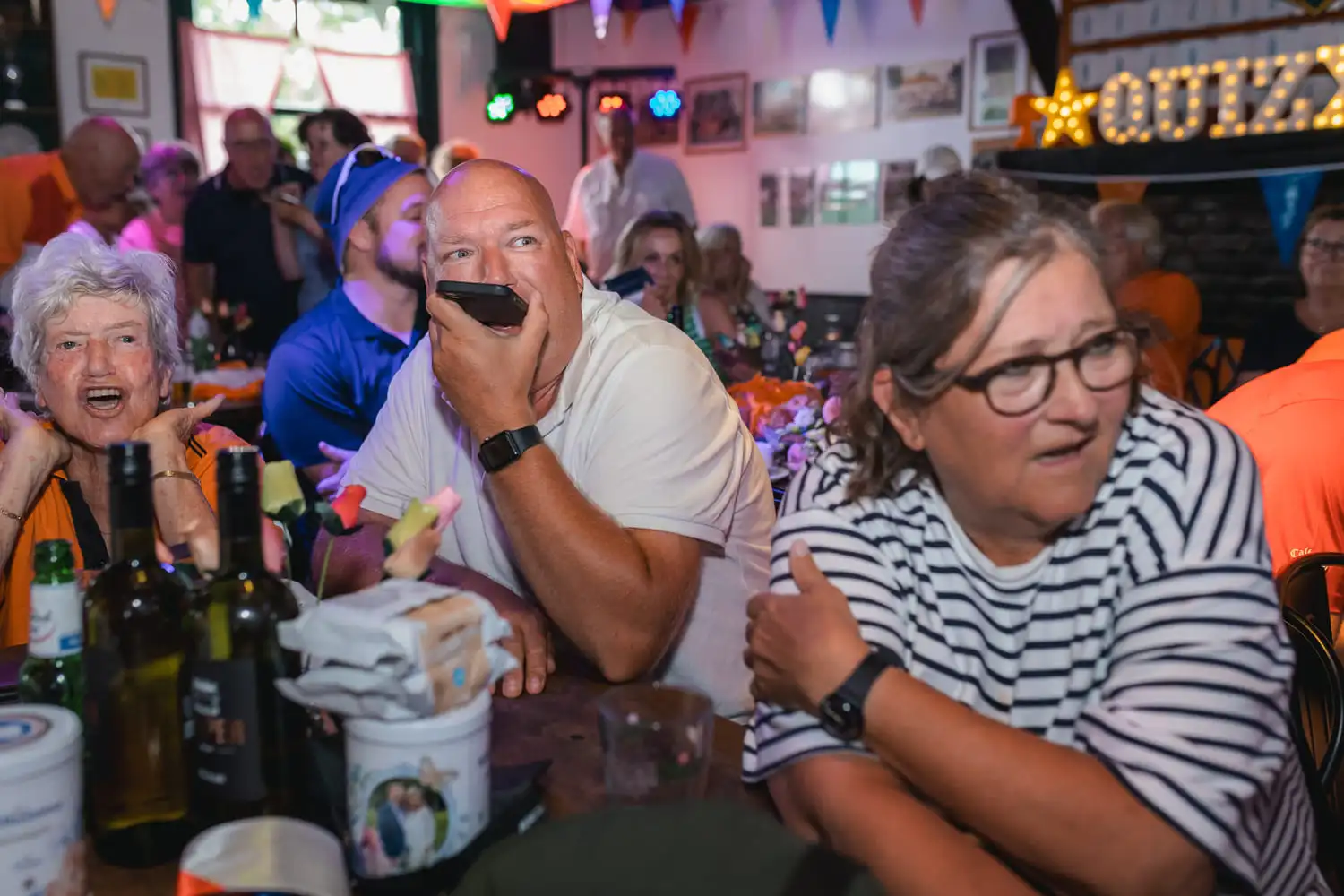 Een levendige pubquiz in Breda met deelnemers aan tafels in een gezellig café, omringd door gekleurde vlaggetjes en een verlicht quizbord.