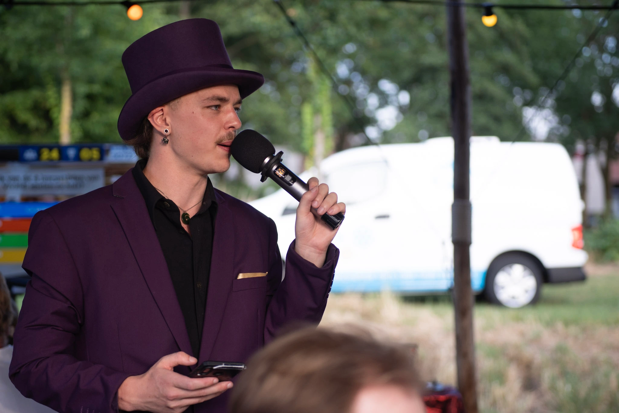 Man in paarse formele kleding met microfoon tijdens een pubquiz in Den Haag.