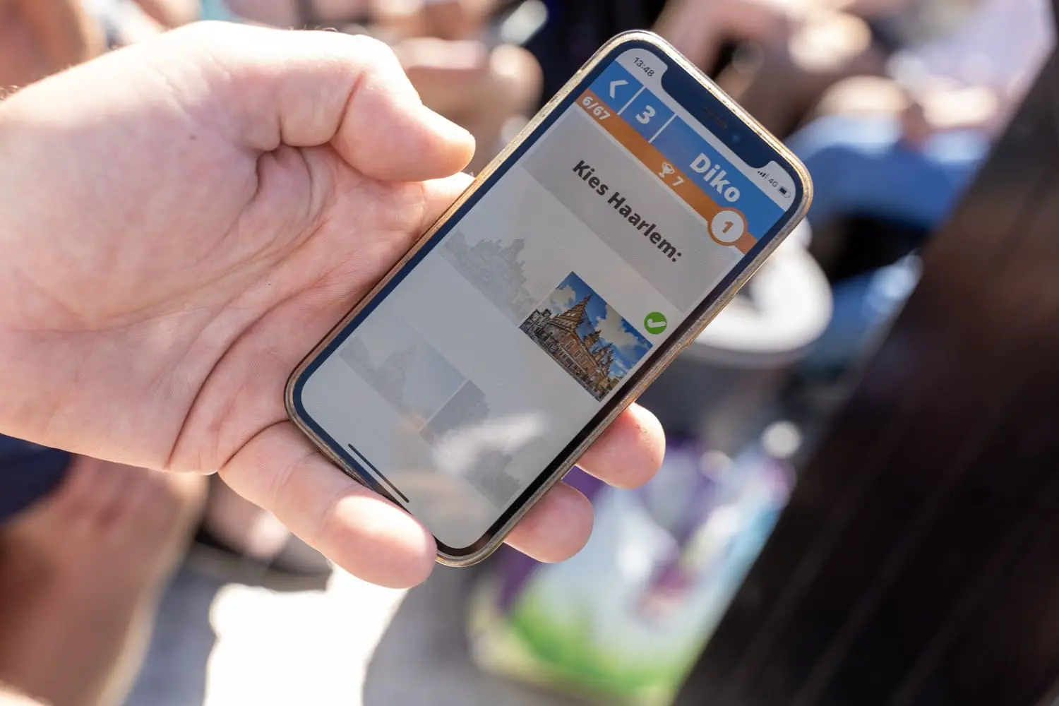 Hand houdt een smartphone vast met daarop een quizvraag over Haarlem tijdens een gepersonaliseerde pubquiz. Ideaal voor interactieve quizactiviteiten.