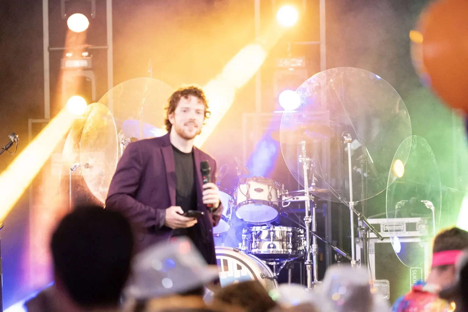 Een quizmaster op een podium met levendige verlichting en een drumstel op de achtergrond, geschikt voor entertainmentavonden en quizmaster inhuren.